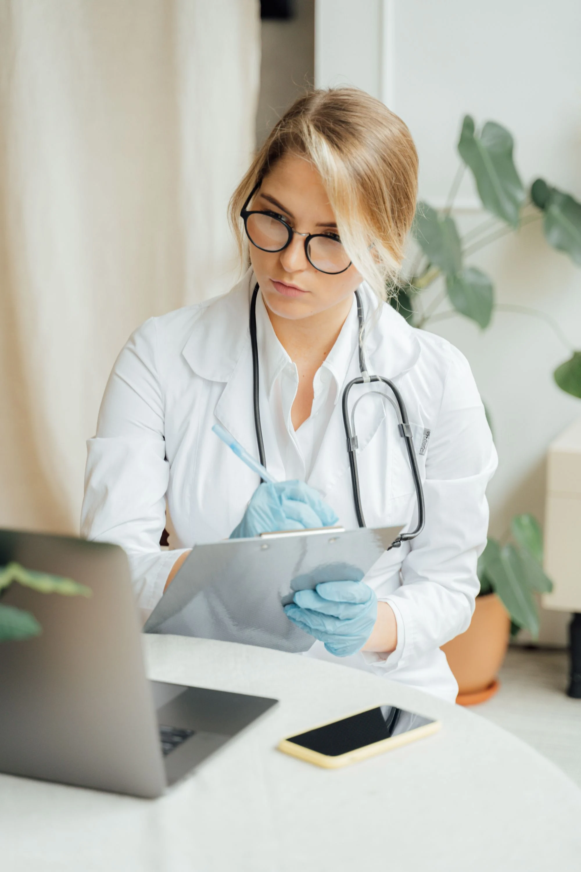 Doctor taking consultation notes beside a laptop